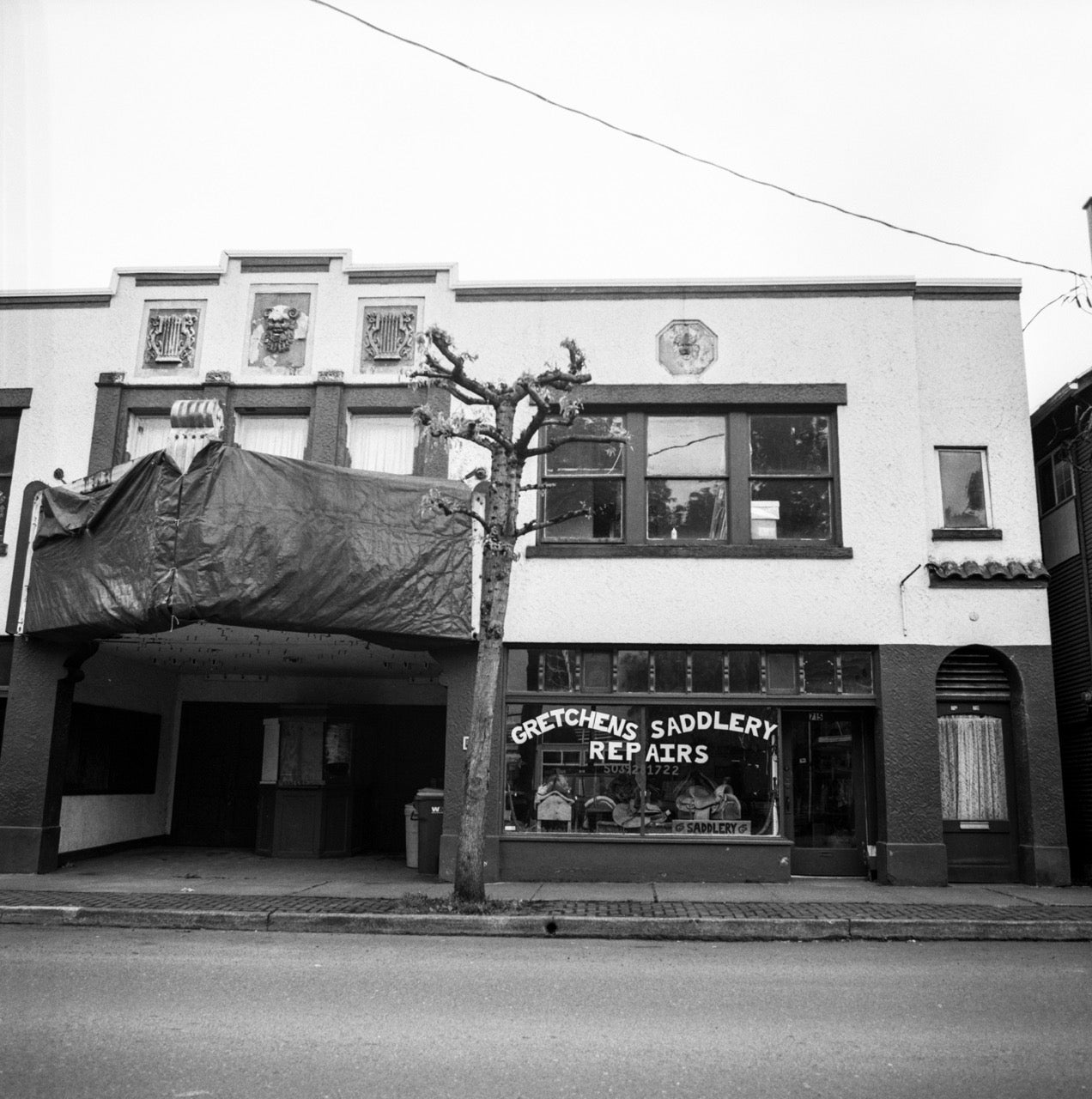 The Joy Theatre building, now closed. The ground floor shows a saddlery store, and there's tarp over the old marquee.